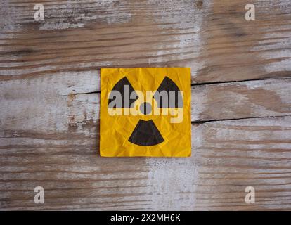 Yellow paper with Radiation warning sign on it on a wooden surface. Stock Photo