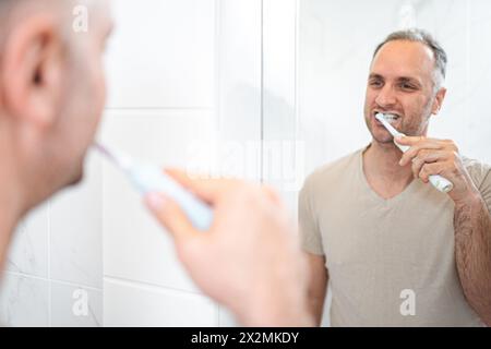 Man brushing his teeth with electric toothbrush in bathroom. Stock Photo