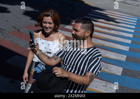 Adult man with beard and hat with young Latin American woman walking through a city on vacation using the map on his cell phone to guide him. Vacation Stock Photo