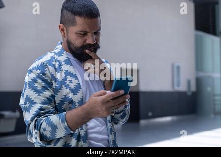 Latin American bearded man in a mall space using his cell phone. Communications concept Stock Photo