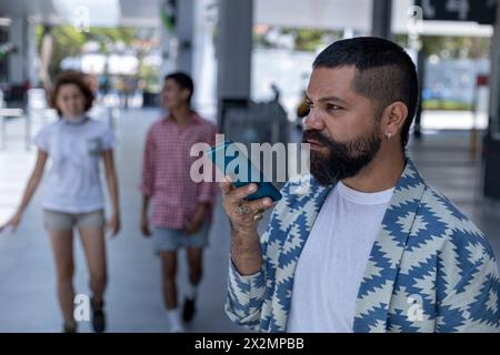 Latin American bearded man in mall spaces using his cell phone to send a voice message. Communications concept Stock Photo