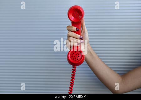 Red handset held by a woman's hand. Gray background. Vintage technology concept. Stock Photo