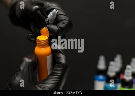 Uncapping a bottle of yellow tattoo ink, background of bottles of different inks and work table. Body art concept Stock Photo