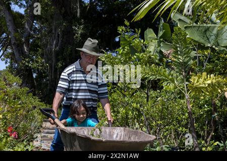 Gardening with children. Grandfather and his Latin American grandson transport a wheelbarrow to work the bushes in their home garden. Hobbies and leis Stock Photo