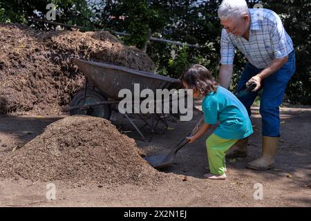 Gardening with children. Grandfather and his Latin American grandson load a wheelbarrow with soil to work in their home garden. Hobbies and leisure, l Stock Photo