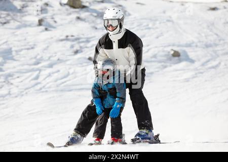 Father supports his child when they slide on alpine skis Stock Photo