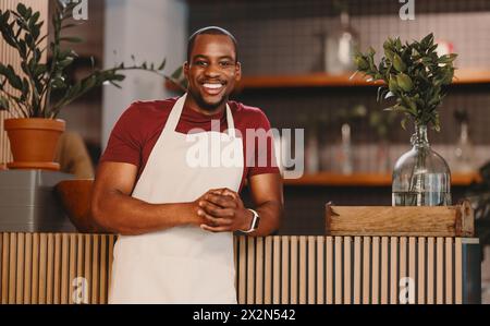 Portrait of a happy male entrepreneur standing confidently in his modern coffee shop. Man in an apron looking at the camera with a welcoming smile, em Stock Photo