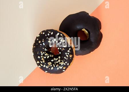 two Chocolate covered donuts with crush nuts on top. zenithal angle on colored background Stock Photo