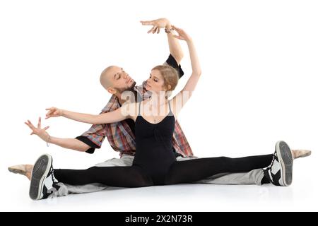 Ballerina in black and bald breakdancer sit on floor and portray puppets isolated on white background. Woman stretched legs in twine. Stock Photo