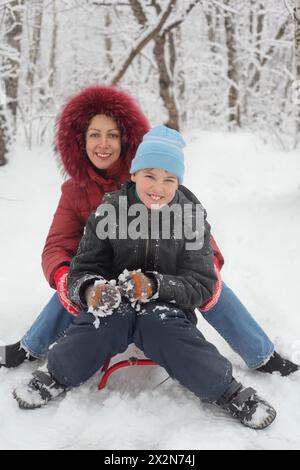 Mother, son ride on sled in winter forest, focus on child Stock Photo