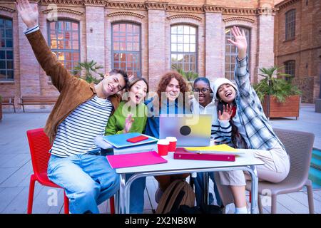 Group Of Smiling Multiracial Students With Laptop Sitting Waving At Camera. Stock Photo