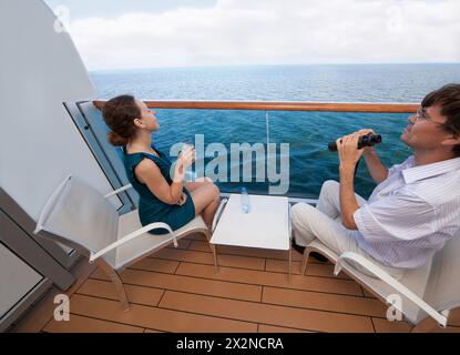 man and woman travel on ship, sit on chairs, drinking water and watching in binoculars Stock Photo