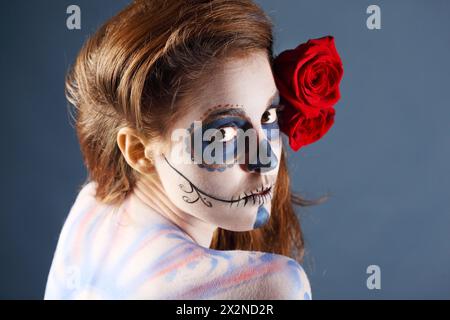 Melancholy zombie girl with painted face and two red roses in her hair looks at camera. Stock Photo