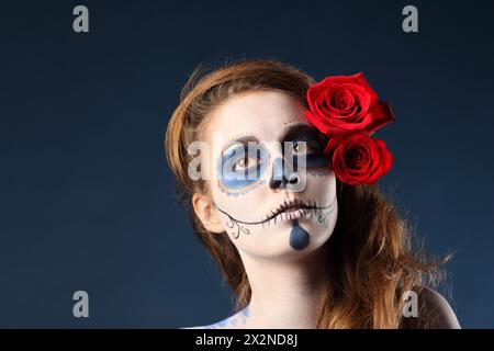 Pretty zombie girl with painted face and two red roses in her hair looks away. Stock Photo