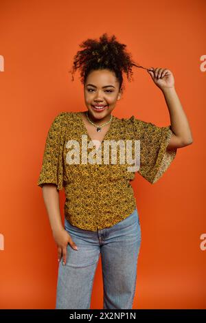 African American woman in stylish attire posing against vivid orange backdrop. Stock Photo