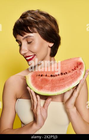 A young woman playfully holds a slice of watermelon in front of her face against a vibrant backdrop. Stock Photo