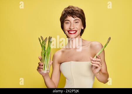 A stylish young woman in a white dress holding a bunch of fresh asparagus. Stock Photo