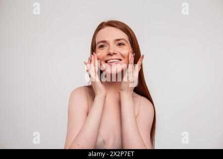 Happy Cute Beauty Fresh Redhead Girl With Smile Smears Cream On Her Face And Does Facial Skin Care. Beauty, Care And Skin Hydration Stock Photo