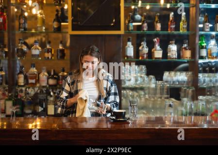 Waitress standing in bar and wiping and polishing beer glass. Bartender woman working in bar counter, preparing and cleaning, work before guests come, Stock Photo