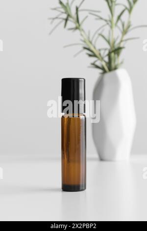 Amber glass roll-on bottle mockup with a rosemary on the white table. Stock Photo