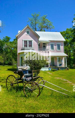 Old house in a North Florida small town is painted an eye-catching pink.  An old, horse-drawn buggy sits in the front yard of the house. Stock Photo