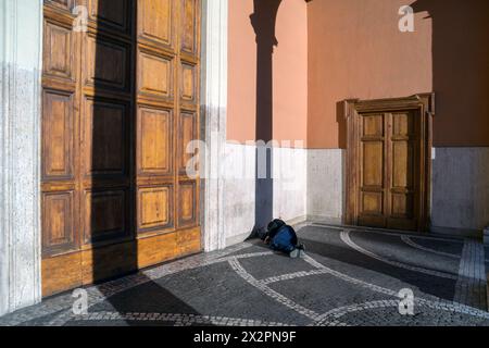 Italy, Rome: a homeless man sleeps lying in the shade of a column in front of the entrance to a closed church Stock Photo