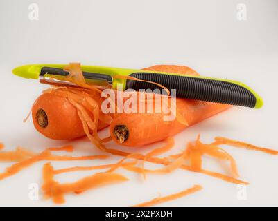 Carrots preparation with a lime green potato vegetable peeler isolated on a white background Stock Photo