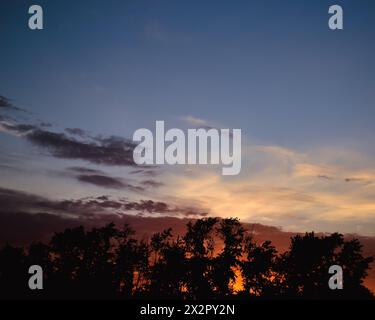 Morning glow illuminates the clouds on a beautiful colorful sky above the silhouettes of trees at dawn Stock Photo