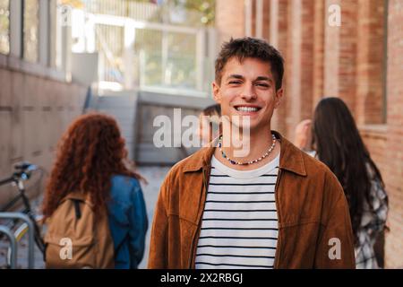 Portrait of one student teenage male smiling and looking at camera at university campus. Guy standing and staring front with positive expression at high school. Confident happy young man at academy. High quality photo Stock Photo