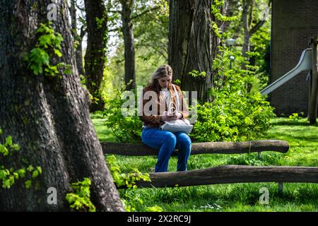 Woman working remotely on her mobile phone in serene park playground. A woman sitting on park bench, engrossed in sending an email from her smartphone Stock Photo