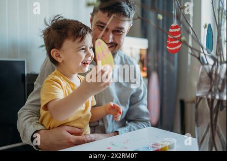 Happy father with son holding painted Easter egg at home Stock Photo