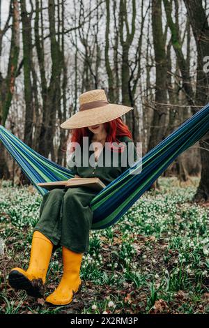Woman reading book near Lily-of-the-valley flowers in forest Stock Photo