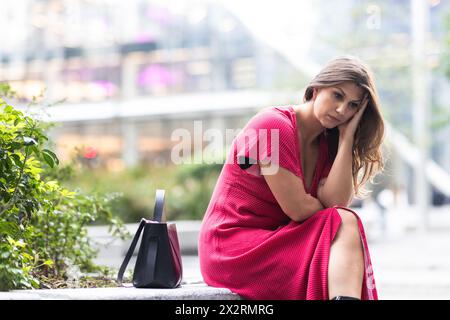 Sad young woman sitting with purse near plants Stock Photo