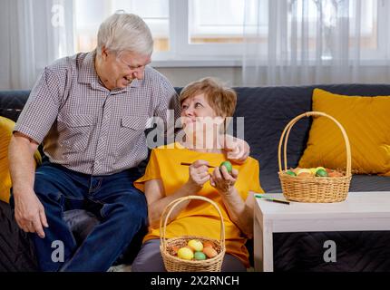 Elderly woman painting Easter eggs near happy man at home Stock Photo