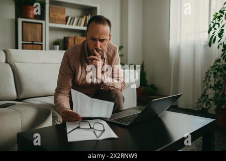 Serious freelancer reading document near laptop at home office Stock Photo