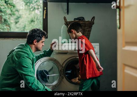 Son loading clothes in washing machine near father at home Stock Photo