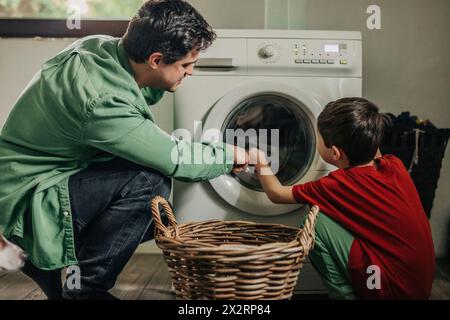 Father and son loading clothes from basket in washing machine at home Stock Photo
