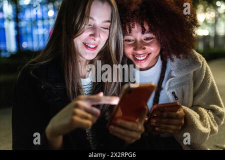 Smiling young women using smart phones at night Stock Photo