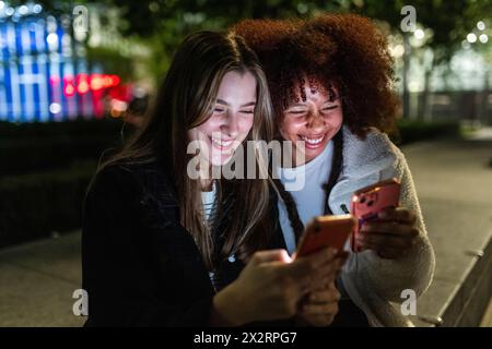 Happy young friends using smart phones at night Stock Photo