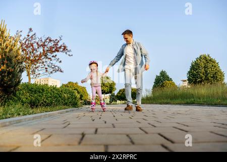 Father holding hand of daughter roller skating on footpath Stock Photo
