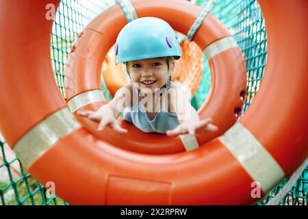 Smiling girl wearing helmet and doing obstacle course at rope park Stock Photo