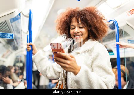 Smiling woman using smart phone in subway train Stock Photo