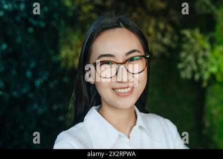 Smiling young businesswoman wearing eyeglasses in front of plants Stock Photo