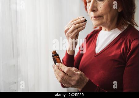 Senior woman smelling essential oil from bottle at home Stock Photo