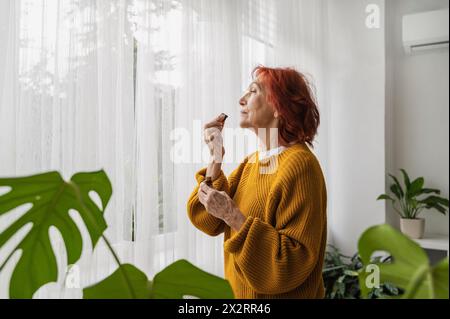 Retired senior woman smelling essential oil from bottle at home Stock Photo