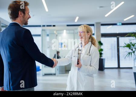 Happy mature doctor shaking hands with man in hospital Stock Photo