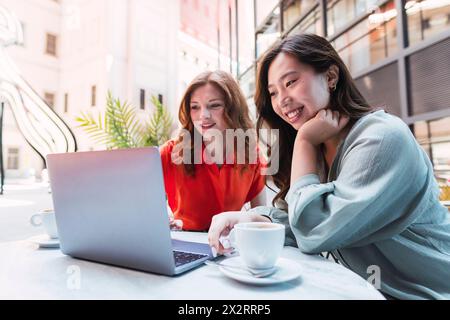 Smiling women using laptop on table sitting at sidewalk cafe Stock Photo