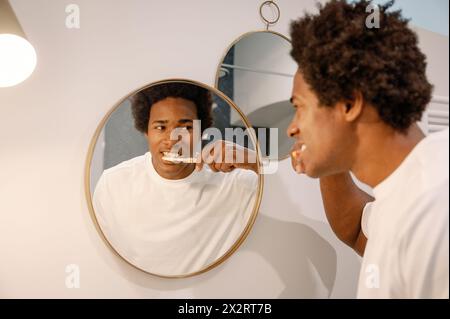 Man brushing teeth looking at mirror reflection in bathroom Stock Photo