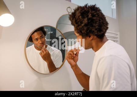 Man brushing teeth looking at mirror in bathroom Stock Photo