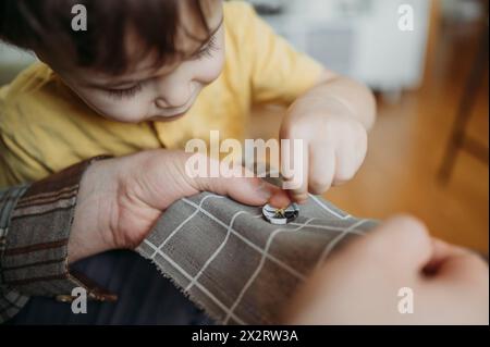 Father teaching son to sew button on cloth Stock Photo